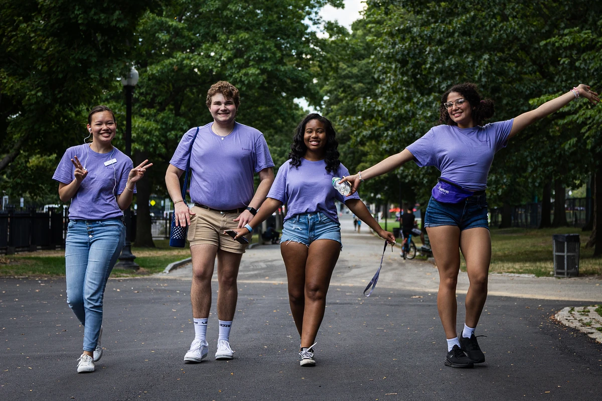 Four people in purple shirts walk joyfully down a tree-lined path.